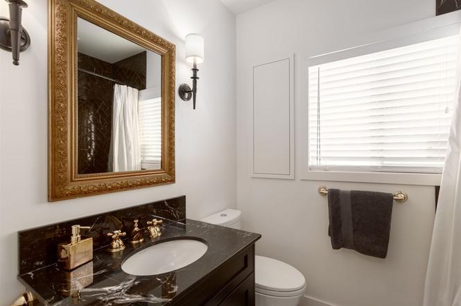 Bathroom after renovation — marble-topped vanity, gilt mirror and brass sconces