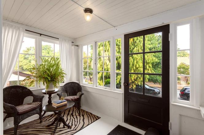 Enclosed front porch after renovation — white floor and panelling, black glazed door and wicker seating